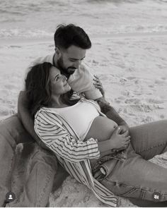 a man and woman are sitting on the beach with their baby in his lap,