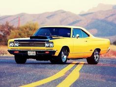 an old yellow car is parked on the side of the road in front of mountains