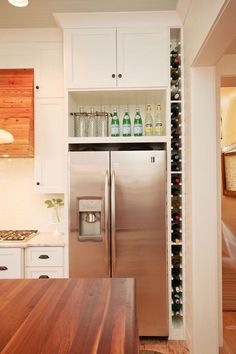 a stainless steel refrigerator in a kitchen with white cabinets and wooden counter tops, along with wine bottles on the shelves