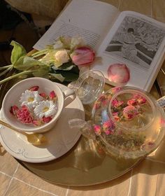 an open book on a table with flowers and teacups in front of it