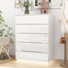 a white chest of drawers sitting next to a chair and potted plant in a living room