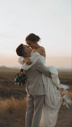 a bride and groom embracing each other in the middle of an open field at sunset