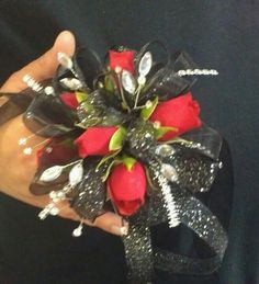 a hand holding a red rose and black ribbon corsage with silver sequins