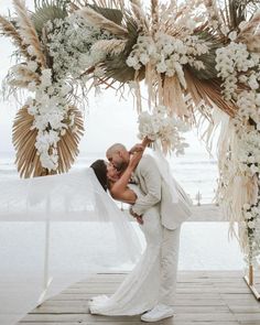 a bride and groom kissing under an outdoor wedding ceremony arch with flowers on the side