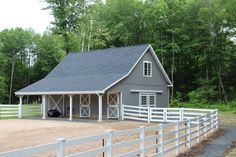 a gray barn with a white fence around it