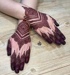 two hands with henna tattoos on them sitting on a wooden floor next to each other