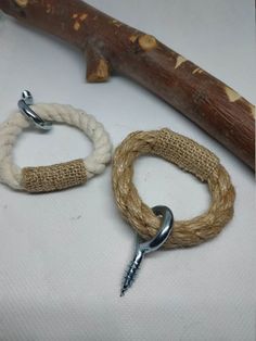 two rope bracelets with metal clasps on white cloth next to a wooden stick