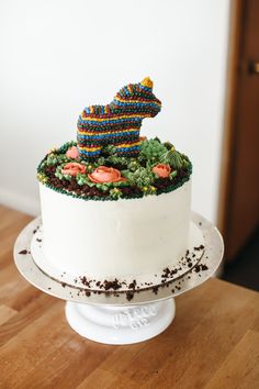 a cake decorated with flowers and an animal topper on a wooden table in front of a white wall