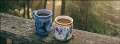 two coffee cups sitting on top of a wooden bench