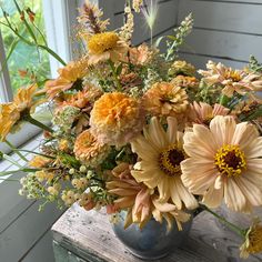 a vase filled with lots of flowers on top of a wooden table next to a window