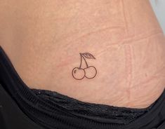 a small cherry tattoo on the side of a woman's stomach, with two cherries attached to it