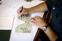 a man sitting at a table working on some designs with his pen and paper in front of him