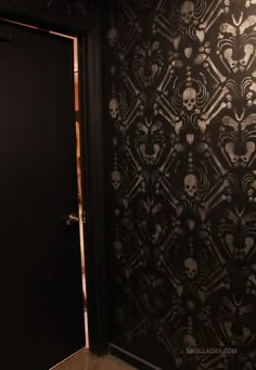 a black door with skulls on it in front of a wallpapered room that is dark