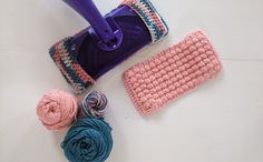 a crocheted scrub cloth, ball of yarn and a purple mop on a white surface