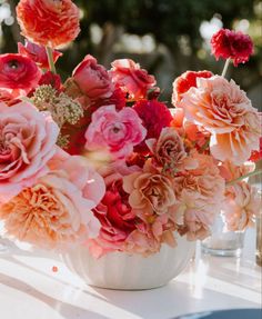 a vase filled with lots of pink and red flowers on top of a white table