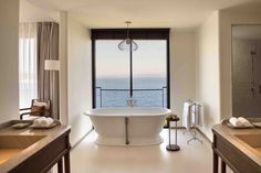 a large white bath tub sitting in a bathroom next to two sinks and a window