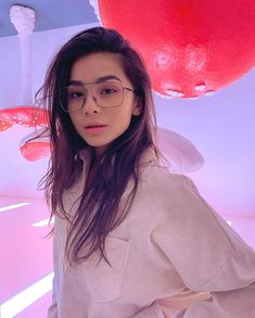 a woman wearing glasses standing in front of red balloons