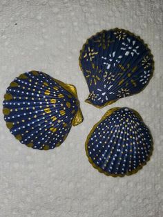 three seashells are sitting on a white towel and one is blue with gold dots