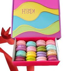 a pink box filled with colorful macaroons on top of a table