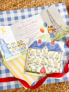 an open book on top of a blue and white checkered table cloth next to a red ribbon