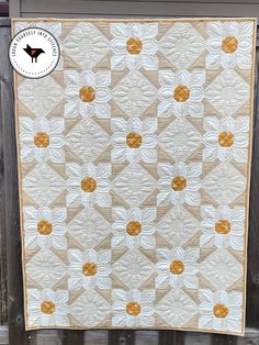 a white and yellow quilt hanging on a wooden fence