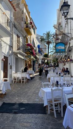 an empty street with tables and chairs set up for dinner in front of white buildings