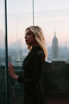 a woman standing in front of a window looking out at the cityscape behind her