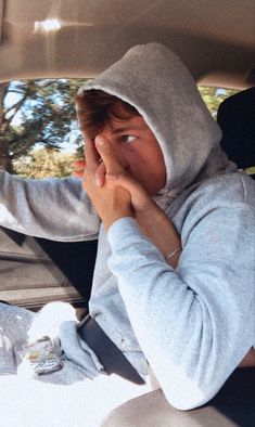 a young boy sitting in the back seat of a car with his hand on his face