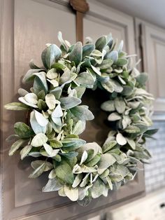 a wreath hanging on the front door of a house with white flowers and green leaves