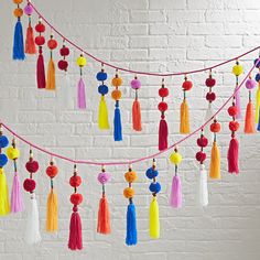 multicolored tassels and pom poms hanging from a string against a white brick wall