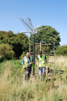 two men in yellow vests standing next to a metal sculpture