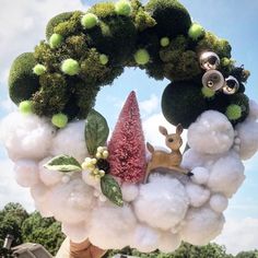 a wreath made out of cotton balls and fake flowers with a deer in the middle