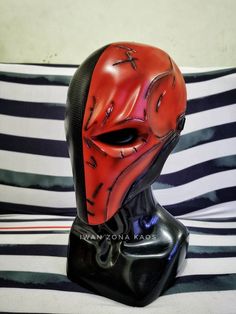 a red mask is on top of a black headdress and striped pillow in the background