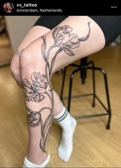 a woman sitting on top of a wooden floor next to a chair with flowers tattooed on her leg