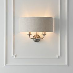 a light fixture mounted on the side of a white wall with a gray fabric shade