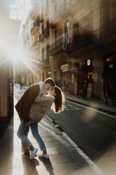 a man and woman kissing on the street in an alleyway with buildings behind them