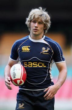 a young man holding a rugby ball on top of a field