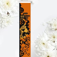 an orange and black cross stitch bookmark next to white flowers