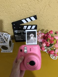 a pink camera sitting on top of a table next to flowers and a movie clap