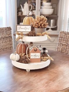 a three tiered tray with pumpkins and other decorations on it, sitting on a dining room table