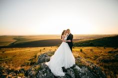 a bride and groom standing on top of a rock in the middle of a field