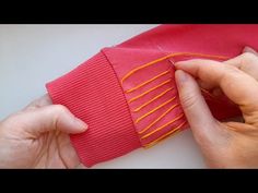 two hands are stitching fabric together on a piece of red material with orange thread