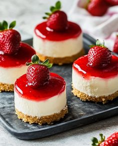 four cheesecakes with strawberries on top are sitting on a black platter