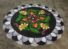 a black and white doily with colorful flowers on the center is sitting on concrete