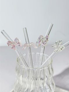 four glass drinking straws in a clear vase on a tray with silver handles and metal tips