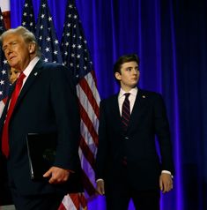 two men in suits and ties standing next to each other with american flags behind them