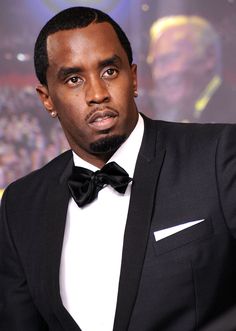 a man in a tuxedo and bow tie looking at the camera with an audience behind him