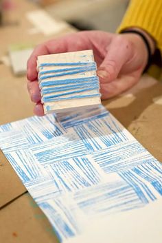 someone is making something out of cardboard with blue and white lines on it, while another person's hand holds the edge of one piece of paper