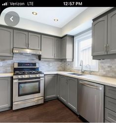 an empty kitchen with stainless steel appliances and wood flooring, along with gray cabinets