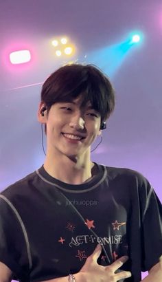 a young man with ear buds on his ears smiles at the camera while standing in front of bright lights